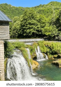 Close view of cascading waterfalls flowing over rocks into a crystal clear river surrounded by lush greenery.