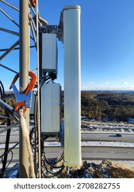 Close view of cellular panel antenna and remote radio units mounted on a mast with traffic and snow below.