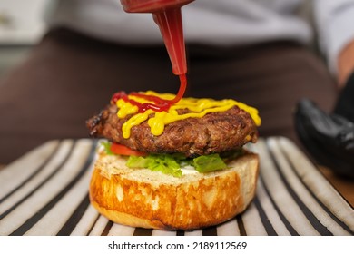 Close up view of a chef adding ketchup on the top of a hamburger in the kitchen of a restaurant