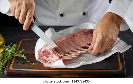 Close Up View Of Chef In White Coat Cutting Lamb Chop With Knife On Wooden Cutting Board