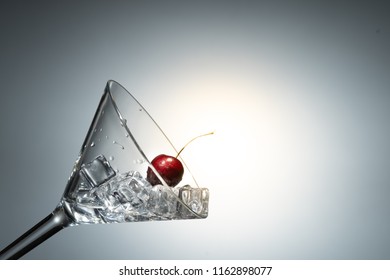 Close up view of cherry among ice in a martini glass in white background with flare .