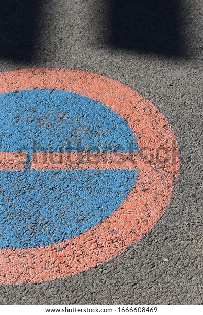 Close up view of a circular traffic sign painted on a\
grey asphalt road. Circular symbol forbidding cars to park at the\
place. Abstract design of a textured surface with red, blue and\
grey colors. 