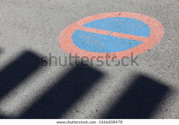 Close up view of a circular traffic sign painted on a\
grey asphalt road. Circular symbol forbidding cars to park at the\
place. Abstract design of a textured surface with red, blue and\
grey colors. 