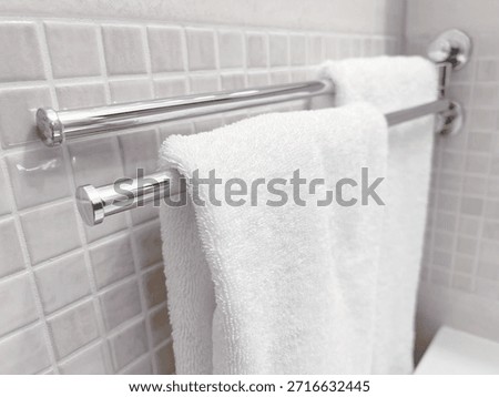 Close up view clean white cotton bath towels hanging on dual chrome metal towel bars mounted on light beige mosaic tiled bathroom wall soft fabric texture domestic washroom amenities home interior styling daily hygiene routine laundry service hotel hospitality travel accommodation comfort