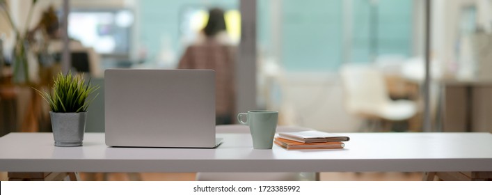 Close up view of comfortable office desk with laptop, mug, tree pot, notebooks and copy space on white table in glass partition office - Powered by Shutterstock