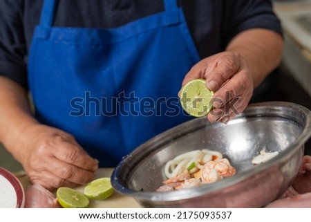 Close up view of a cook adding lemon to a bowl of ceviche ingredients in a restaurant kitchen