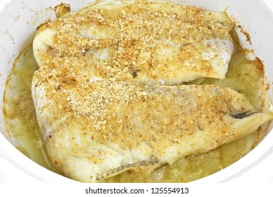 A Close View Of Cooked Breaded Haddock Atop Onions In A Baking Dish.