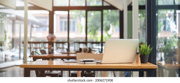 Close up view of co-working space table at cafe with laptop, stationery and blurry cafe interior in the background - Shutterstock ID 2006271908