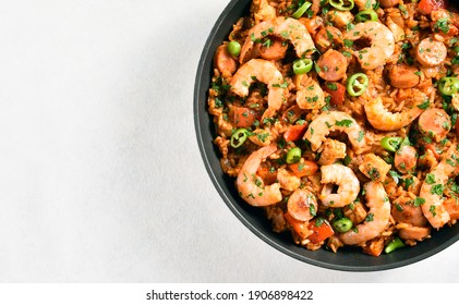 Close up view of creole jambalaya with chicken, smoked sausages and vegetables in frying pan on white stone background with copy space. Top view, flat lay, close up