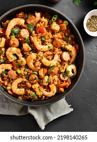 Close Up View Of Creole Style Jambalaya With Prawn, Smoked Sausages And Vegetables In Cooking Pan Over Black Stone Background. Top View, Flat Lay