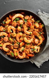 Close Up View Of Creole Style Jambalaya With Prawn, Smoked Sausages And Vegetables In Cooking Pan Over Black Stone Background. Top View, Flat Lay