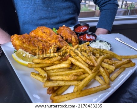 Close up view of crispy fish and chips on a table at a restaurant in front of a Caucasian man