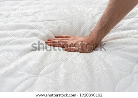 Close up view of cropped hand pressing on soft orthopedic memory foam mattress. Man testing comfortable bed with ecologic material on hypoallergenic topper. Healthy sleeping and advertising concept