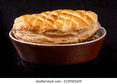 Close Up View Of A Crusty British Pub Steak And Kidney Pot Pie In A Brown Casserole Dish On A Black Table