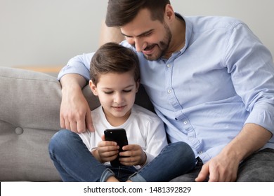 Close up view dad with son sit on couch watching videos on smartphone, different age brothers using app, enjoy time together, parental control, modern wireless tech usage of younger generation concept - Powered by Shutterstock