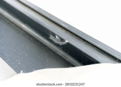 A close up view of a damaged black window frame showing visible white scratches on the surface.