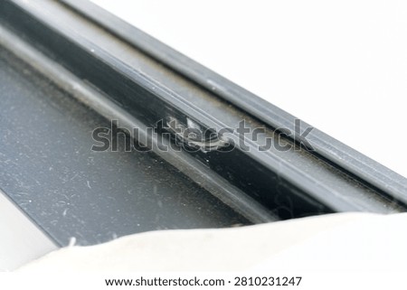 A close up view of a damaged black window frame showing visible white scratches on the surface.
