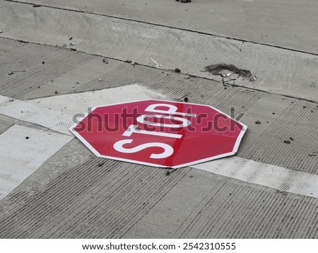 A close up view of a damaged octagonal red STOP sign on a gray concrete surface. The sign’s edges show some signs of damage.