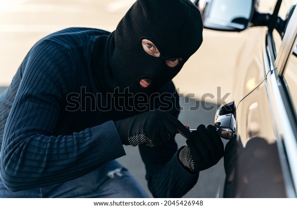 Close up view of the dangerous man dressed\
in black with a balaclava on his head picks the lock with a pick\
while stealing. Car thief, car theft concept\
