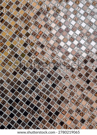 Close up view of decorative mosaic tile pattern featuring small square ceramic pieces in various shades of brown, beige, white, and black, creating textured and intricate geometric design surface
