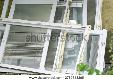 close up view of disassembled plastic windows stacked outside after being removed from a building with white frames glass window panes built in blinds and remaining yellow polyurethane foam. 