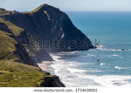 Close view of a dramatic coastal cliff face descending into breaking Pacific Ocean surf below.