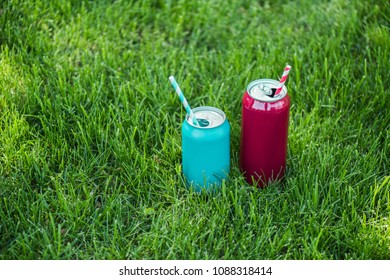 close up view of drinks in cans with straws on green grass