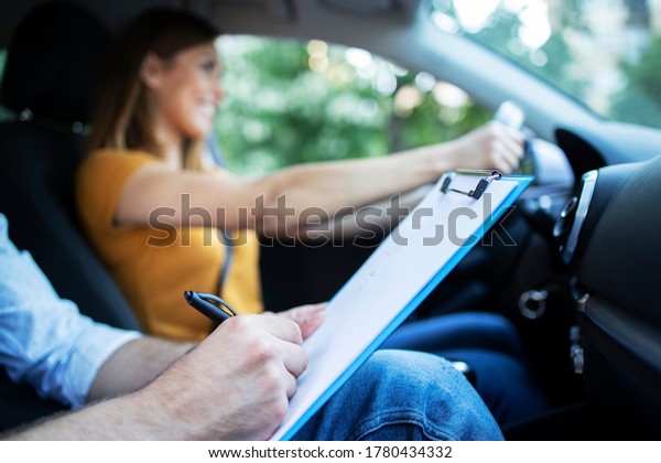 Close up view of driving instructor holding\
checklist while in background female student steering and driving\
car. Acquiring driver\'s\
license.