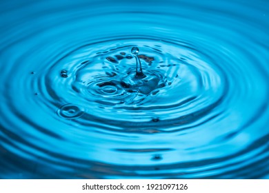 Close Up View Of Drops Making Circles On Blue Water Surface Isolated On Background.