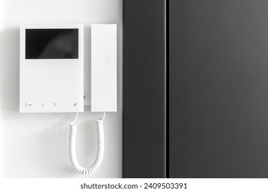 Close up view of electronic doorbell with buttons and copy space display on white wall. Black metal door near intercom device. Concept of smart home protection, privacy and safety in apartment.