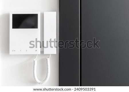 Close up view of electronic doorbell with buttons and copy space display on white wall. Black metal door near intercom device. Concept of smart home protection, privacy and safety in apartment.