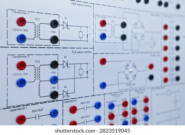 Close view of an electronic training panel with transformer and rectifier circuit diagrams, connectors, and lab equipment for electrical education.