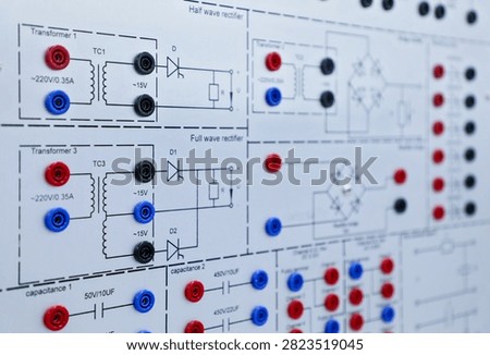 Close view of an electronic training panel with transformer and rectifier circuit diagrams, connectors, and lab equipment for electrical education.