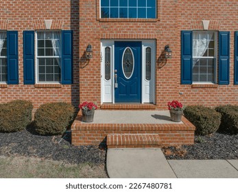 Close up view of elegant blue wooden door with oval stained window, with white sidelights, silver brass color door knob, iron wall light on red brick facade