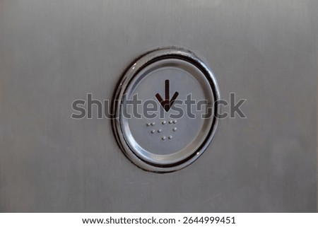 Close up view of an elevator button with downward arrow and braille dots on metal panel