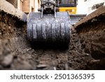 Close up view of excavator bucket digging ground on construction site.