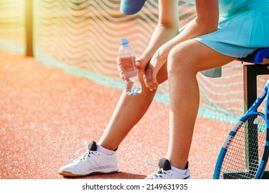 Close Up View Of An Exhausted Tennis Girl Resting On A Plastic Chair Bench On An Outdoor Tennis Court. Lit By An Evening Sun. No Face, Bent Forward.