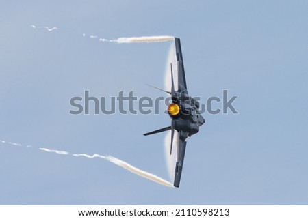 Close view of a F-35C Lightning II  in a high G maneuver, with condensation clouds over the wings and  trails at the wing tips, and afterburner on