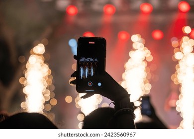 Close view of a fan using a modern cellphone to record a live concert.