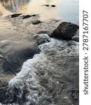Close up view of fast river rapids in Lyngdal, Norway with whitewater foam flowing over dark rocks, showing powerful Nordic nature.