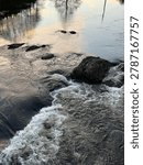 Close up view of fast river rapids in Lyngdal, Norway with whitewater foam flowing over dark rocks, showing powerful Nordic nature.