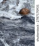 Close up view of fast river rapids in Lyngdal, Norway with whitewater foam flowing over dark rocks, showing powerful Nordic nature