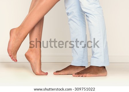 Close up view of the feet of a barefoot man and a woman standing on tiptoe facing one another suggestive of a romantic liaison