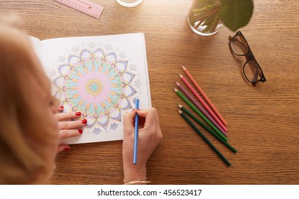 Close Up View Of Female Drawing In Adult Coloring Book With Color Pencils On Table At Home. Anti Stress Adult Colouring Book.