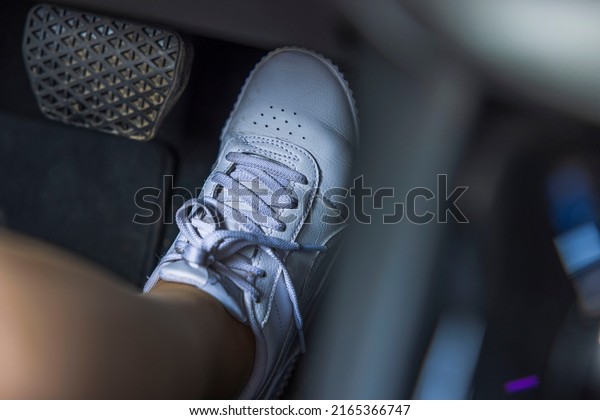 Close up view of female foot in white\
sneakers on electric vehicle gas pedal.\
Sweden.