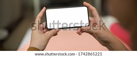 Close up view of female freelancer relaxing with horizontal mock-up smartphone in home office 