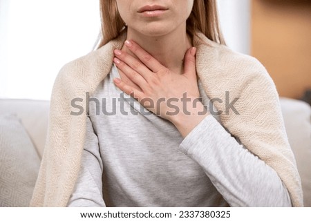 Close up view of female hand on neck, suffering from sore throat. Cropped view of sick woman feel discomfort in chest, painful, difficult to swallow. Concept of tonsillitis, angina, pectoris
