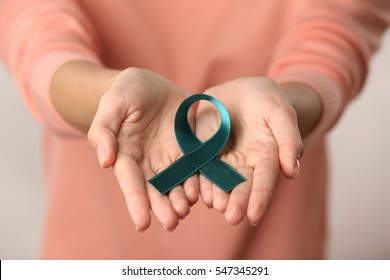 Close up view of female hands holding sea-green ribbon. Ovarian cancer and gynecological disorders concept
