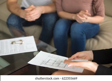 Close up view of female realtor showing to young couple of buyers flat plan on the sheet of paper sitting on sofa indoors, discussing buying apartment, considering flat purchase, interior layout  - Powered by Shutterstock