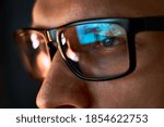 Close up view of focused businessman wears computer glasses for reducing eye strain blurred vision looking at pc screen with computer reflection using internet, reading, watching, working online late.